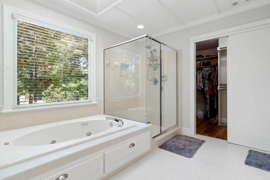 Bright bathroom featuring a glass shower, tub, and a walk-in closet with clothes.