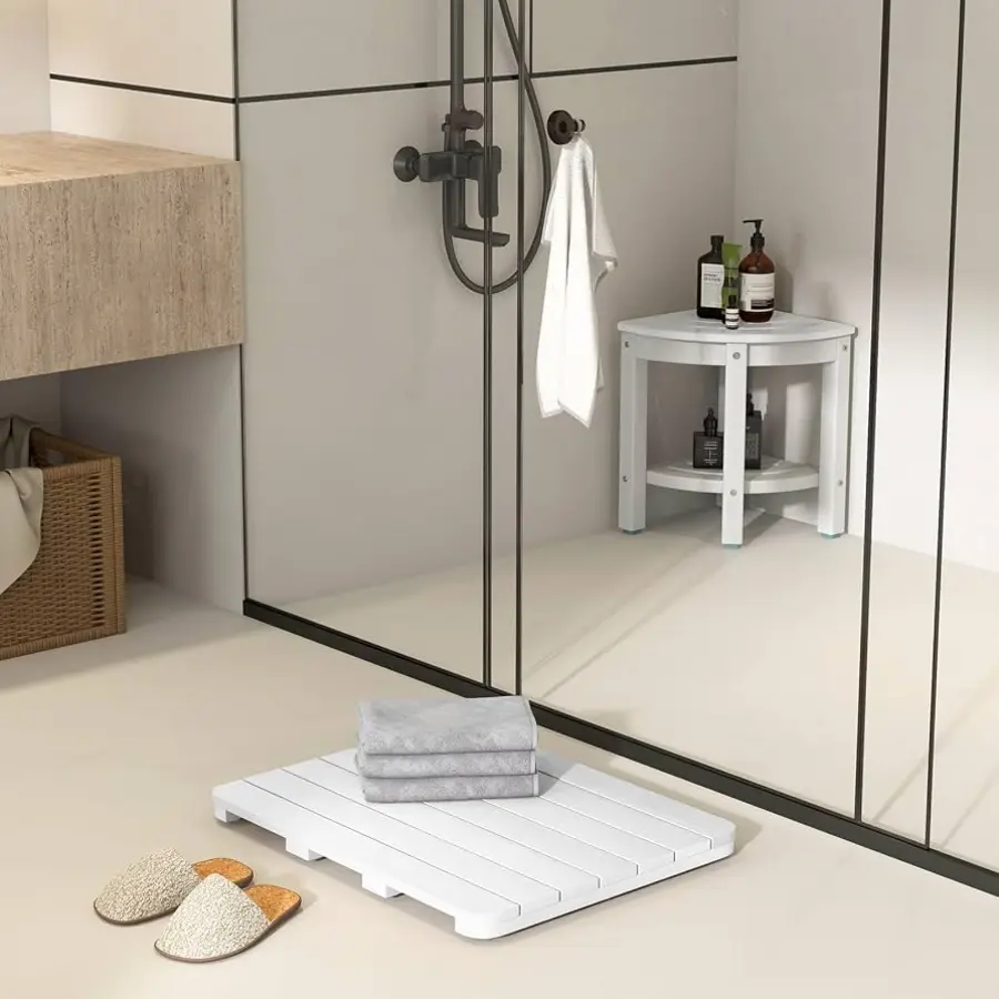 A modern bathroom featuring a white bath mat outside a walk-in shower, with towels and a small shelf.