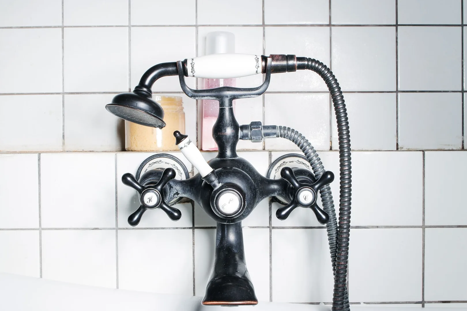 White bathroom tiles with dark grout behind a black shower fixture.