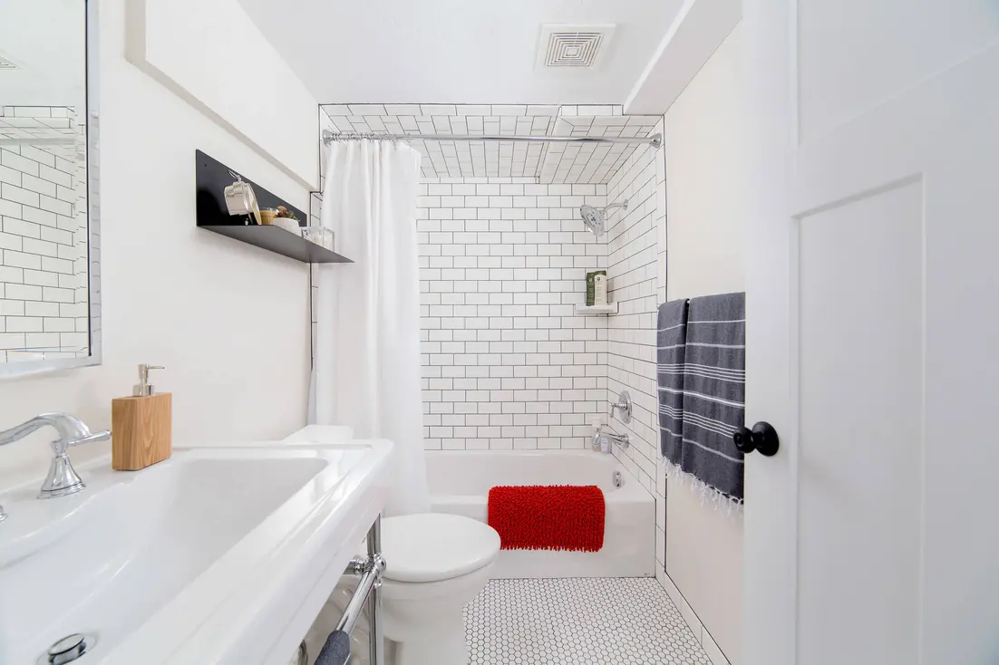Clean bathroom featuring a white tiled shower, a bathtub, and a red bath mat.