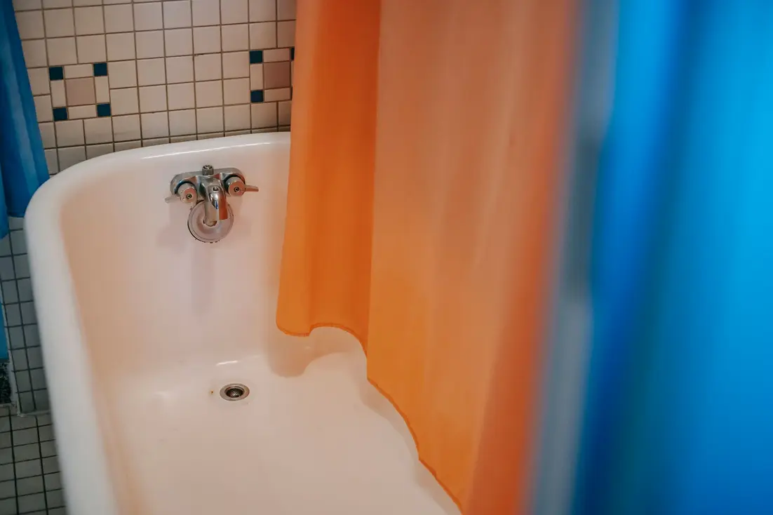 A corner bathtub with orange and blue shower curtains in a tiled bathroom.