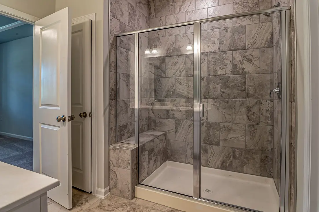 Clear glass shower door in a modern bathroom, partially open, with white tiled walls and floor.